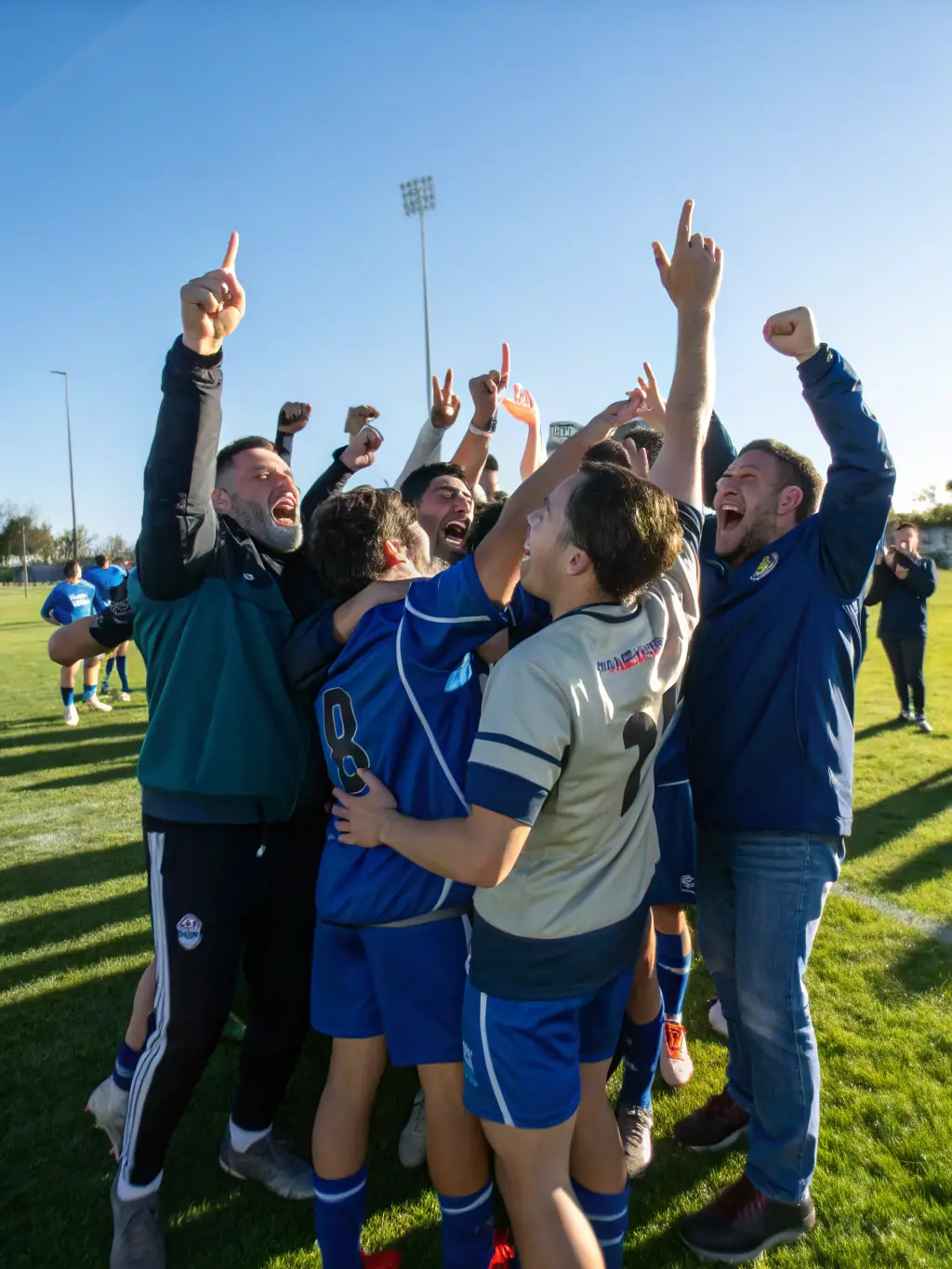 A group of young football players celebrating a goal during a match, showcasing teamwork and camaraderie, set against a vibrant green field.